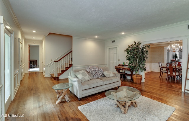 living room featuring hardwood / wood-style flooring, a textured ceiling, ornamental molding, and an inviting chandelier