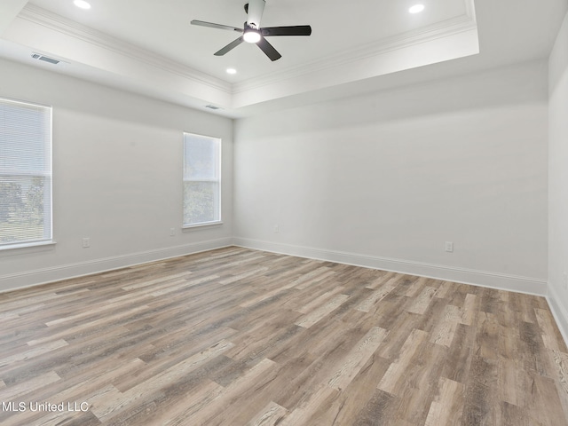 spare room with ornamental molding, ceiling fan, light wood-type flooring, and a raised ceiling