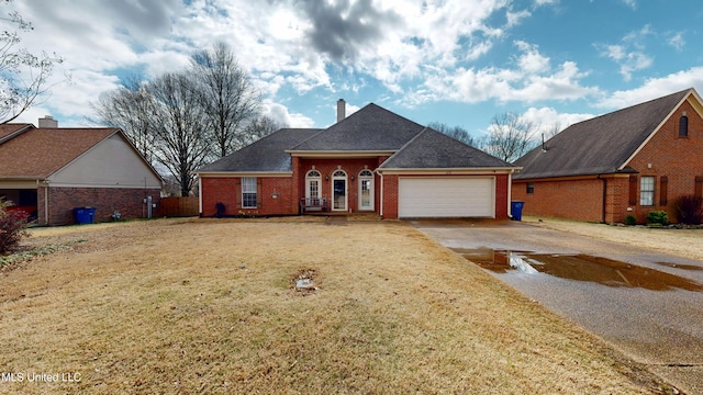 view of front of home featuring brick siding, a front lawn, a chimney, a garage, and driveway