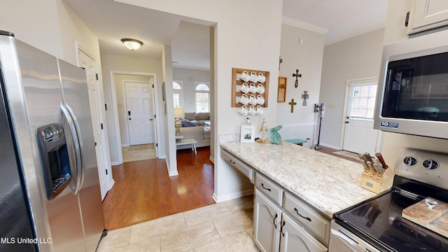 kitchen featuring ornamental molding, white cabinetry, stainless steel appliances, light tile patterned floors, and baseboards