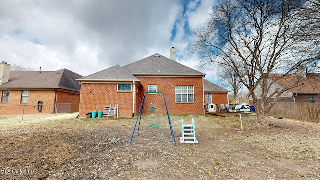 rear view of house with fence, brick siding, roof with shingles, and a chimney