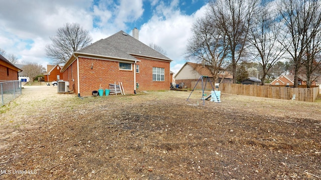 back of property with fence, a shingled roof, a chimney, central air condition unit, and brick siding