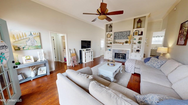 living area featuring wood finished floors, lofted ceiling, ceiling fan, a glass covered fireplace, and crown molding