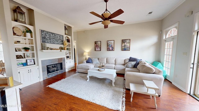 living area with a ceiling fan, crown molding, wood finished floors, and a tile fireplace