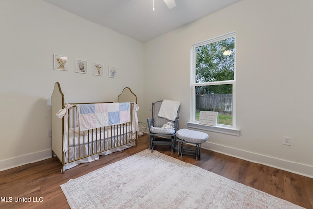 bedroom with a nursery area, dark hardwood / wood-style flooring, multiple windows, and ceiling fan