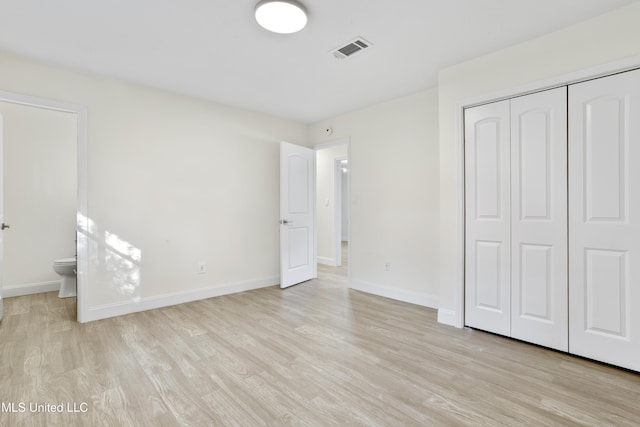 unfurnished bedroom with ensuite bath, light wood-type flooring, and a closet