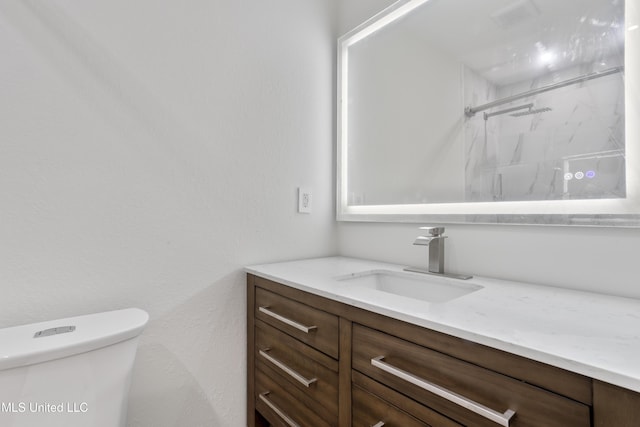 bathroom with toilet, a tile shower, and vanity