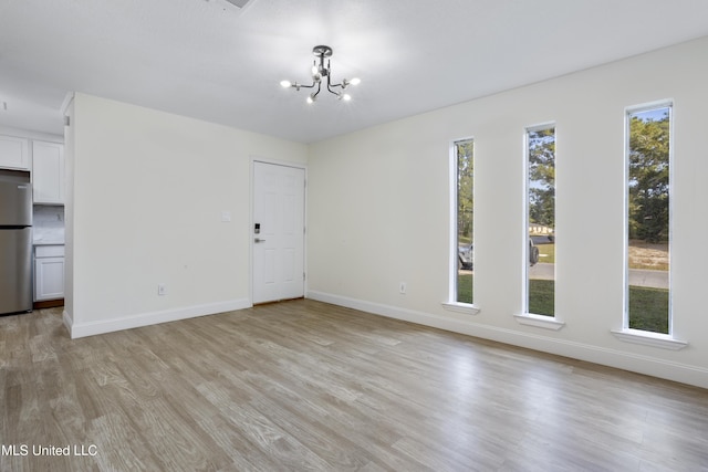 unfurnished living room with an inviting chandelier and light hardwood / wood-style floors