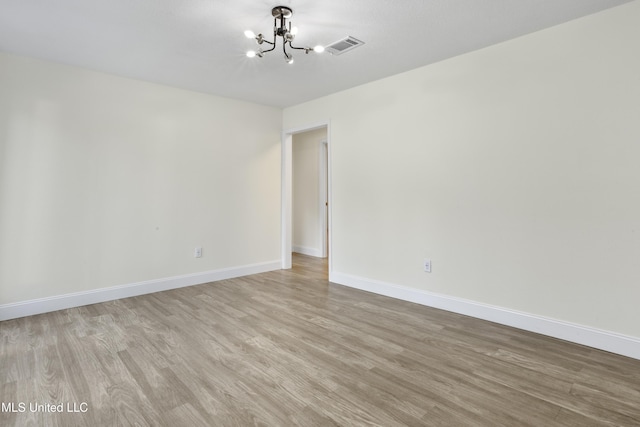 empty room with light wood-type flooring and a notable chandelier