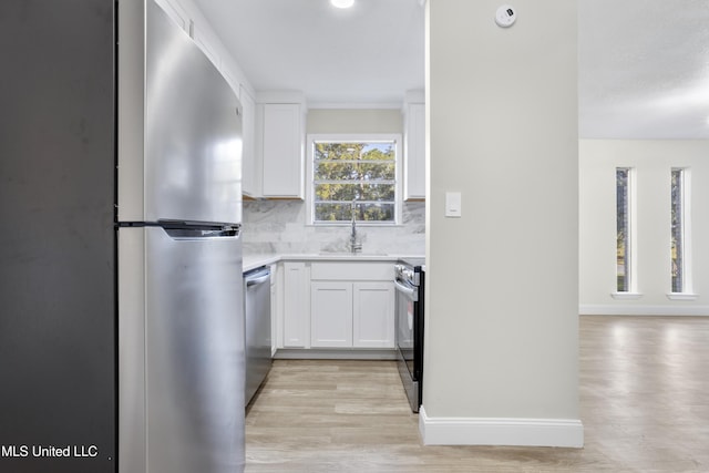 kitchen featuring appliances with stainless steel finishes, white cabinetry, tasteful backsplash, light hardwood / wood-style floors, and sink