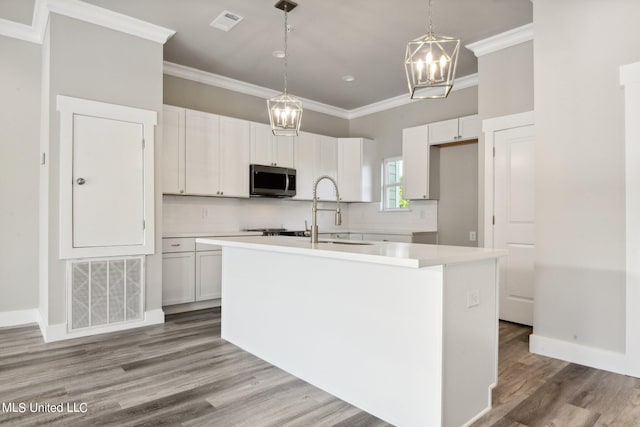 kitchen with crown molding, hanging light fixtures, white cabinets, a center island with sink, and decorative backsplash