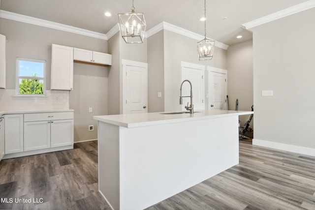 kitchen featuring sink, white cabinetry, ornamental molding, a center island with sink, and decorative light fixtures