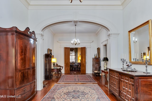 hallway with decorative columns, crown molding, hardwood / wood-style floors, and an inviting chandelier