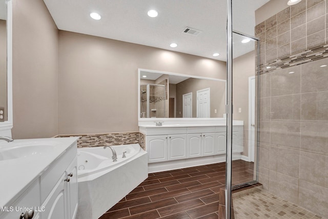 full bath featuring two vanities, visible vents, a sink, and a jetted tub