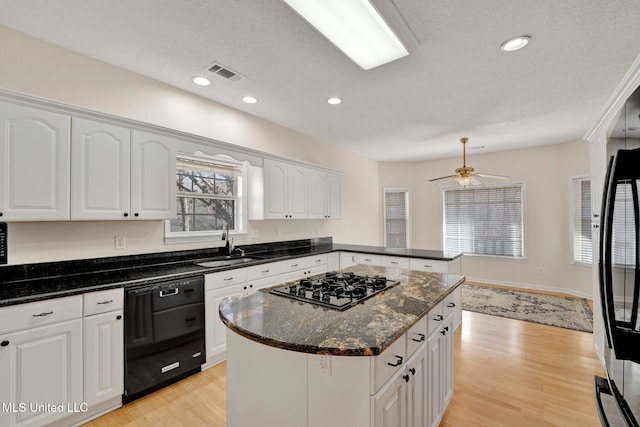 kitchen featuring a sink, visible vents, white cabinets, black appliances, and dark stone countertops