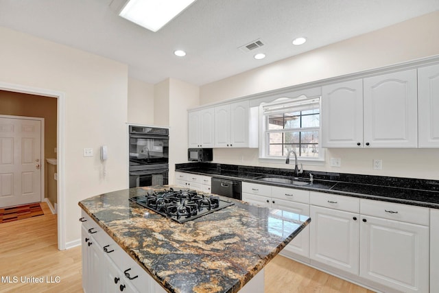 kitchen with dark stone counters, black appliances, a sink, and white cabinets