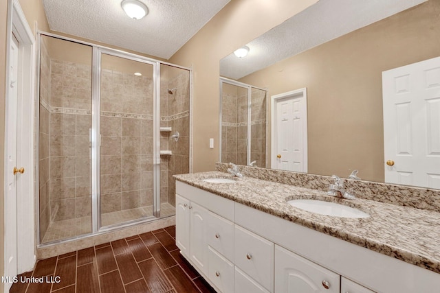 bathroom featuring wood finish floors, a sink, a shower stall, and a textured ceiling