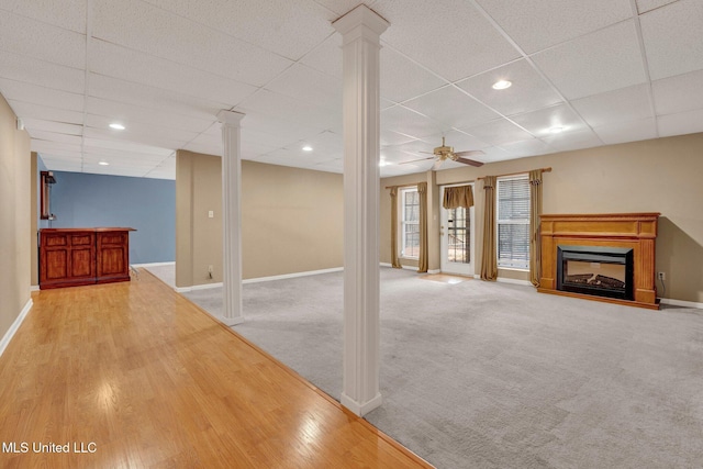 below grade area featuring ceiling fan, a paneled ceiling, light carpet, a fireplace, and baseboards