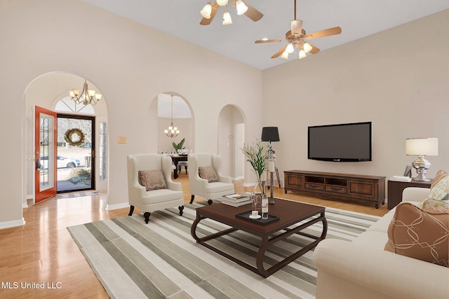 living room featuring light wood-type flooring, baseboards, a high ceiling, and arched walkways