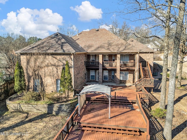 rear view of house featuring a balcony, brick siding, a shingled roof, fence, and stairs