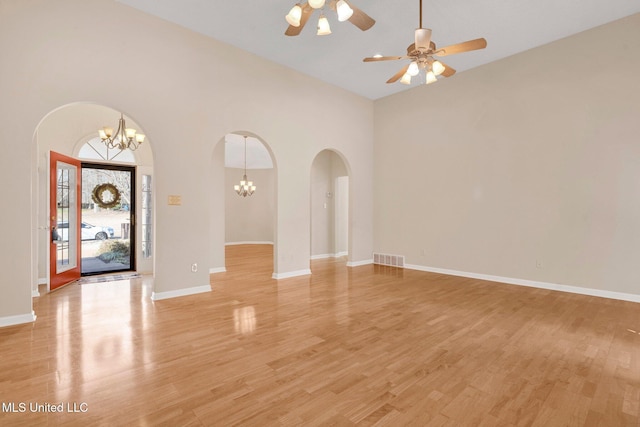 unfurnished living room featuring arched walkways, visible vents, light wood-style flooring, and baseboards