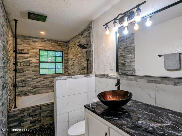 bathroom with vanity, toilet, a textured ceiling, and tile walls