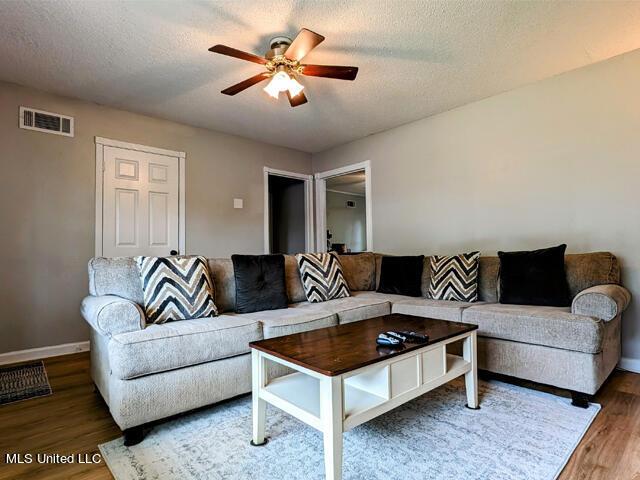 living room featuring a textured ceiling, ceiling fan, and dark wood-type flooring