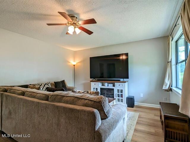 living room featuring ceiling fan, light hardwood / wood-style flooring, and a textured ceiling