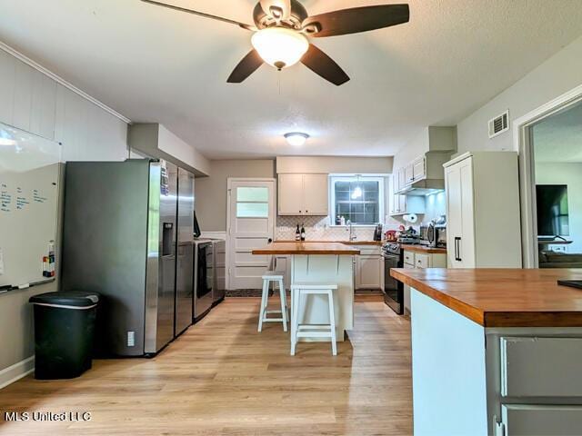 kitchen with stainless steel appliances, a kitchen island, a kitchen breakfast bar, butcher block countertops, and white cabinets