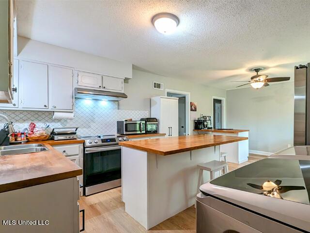 kitchen with butcher block counters, sink, stainless steel appliances, light hardwood / wood-style floors, and white cabinets