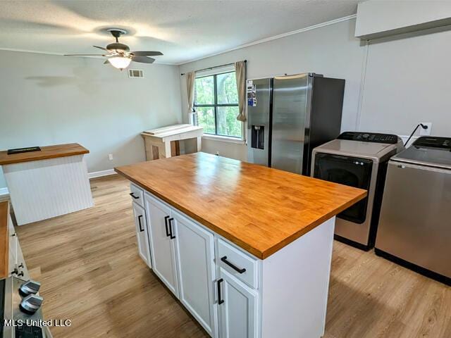 kitchen featuring light wood-type flooring, ceiling fan, stainless steel fridge with ice dispenser, washing machine and dryer, and white cabinetry