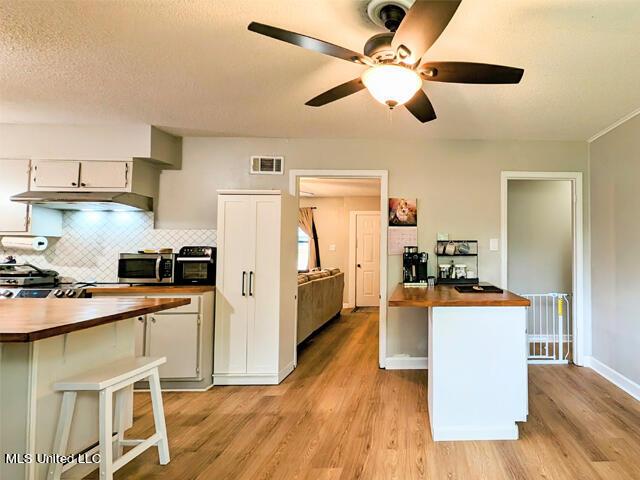 kitchen with wooden counters, a textured ceiling, ceiling fan, light hardwood / wood-style flooring, and white cabinetry