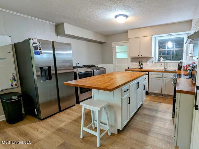 kitchen with washing machine and clothes dryer, sink, wood counters, stainless steel fridge, and white cabinets