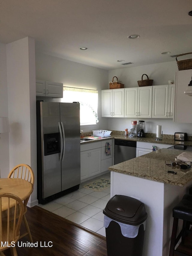 kitchen with kitchen peninsula, stainless steel appliances, stone countertops, white cabinets, and light hardwood / wood-style floors