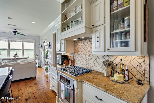 kitchen with crown molding, hardwood / wood-style flooring, appliances with stainless steel finishes, white cabinetry, and light stone counters