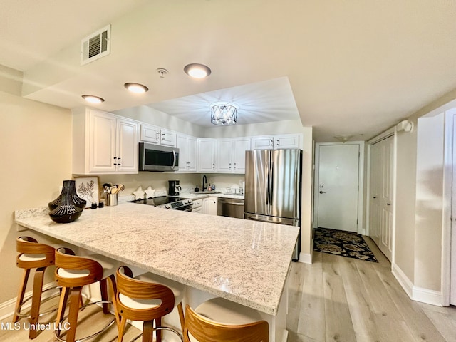 kitchen featuring kitchen peninsula, appliances with stainless steel finishes, a breakfast bar, white cabinetry, and light hardwood / wood-style floors