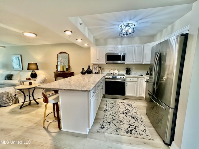 kitchen with light stone countertops, a kitchen bar, kitchen peninsula, stainless steel appliances, and white cabinets