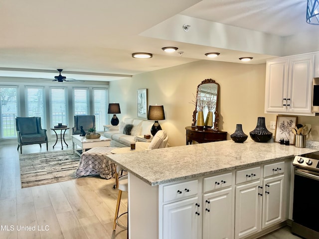 kitchen with electric range oven, white cabinets, light wood-type flooring, and a wealth of natural light