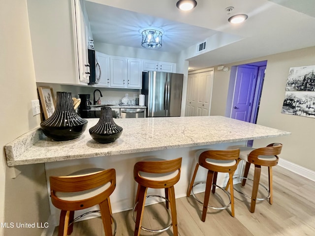 kitchen with appliances with stainless steel finishes, a kitchen bar, white cabinets, and light hardwood / wood-style floors