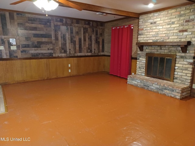 unfurnished living room with wood walls, a brick fireplace, ceiling fan, ornamental molding, and beamed ceiling