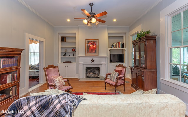 living room featuring light hardwood / wood-style floors, ornamental molding, built in shelves, and ceiling fan