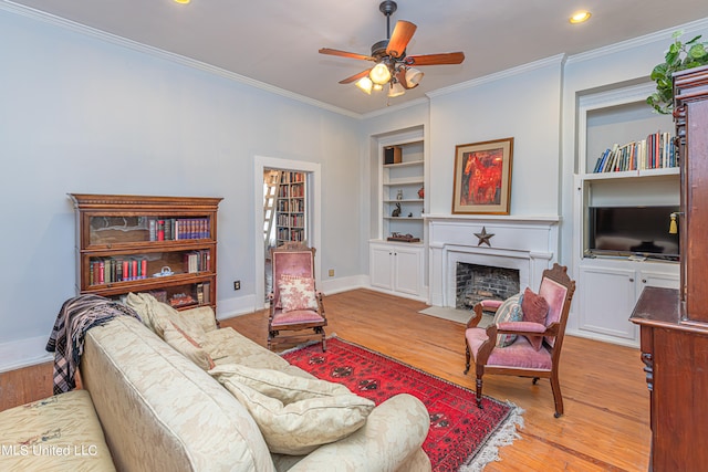 living room with ceiling fan, ornamental molding, light wood-type flooring, and built in shelves