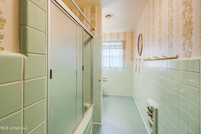 bathroom featuring tile walls, tile patterned flooring, bath / shower combo with glass door, and heating unit