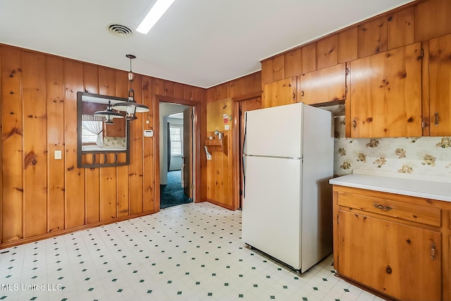 kitchen featuring hanging light fixtures, white fridge, and wood walls