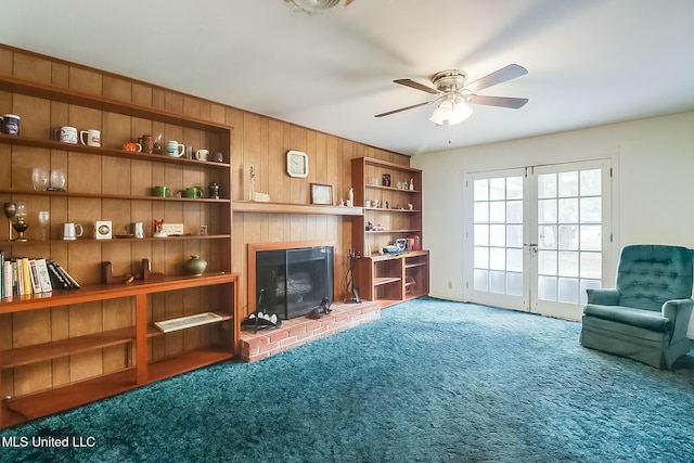 sitting room with french doors, ceiling fan, a brick fireplace, carpet floors, and wood walls