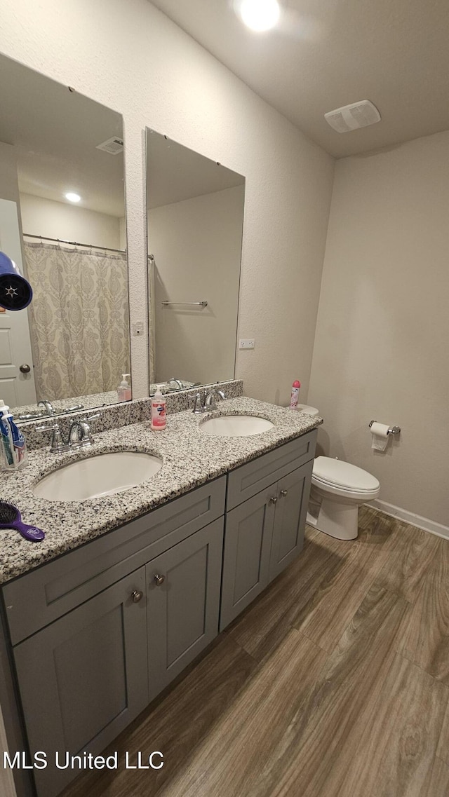full bathroom with double vanity, wood finished floors, toilet, and a sink