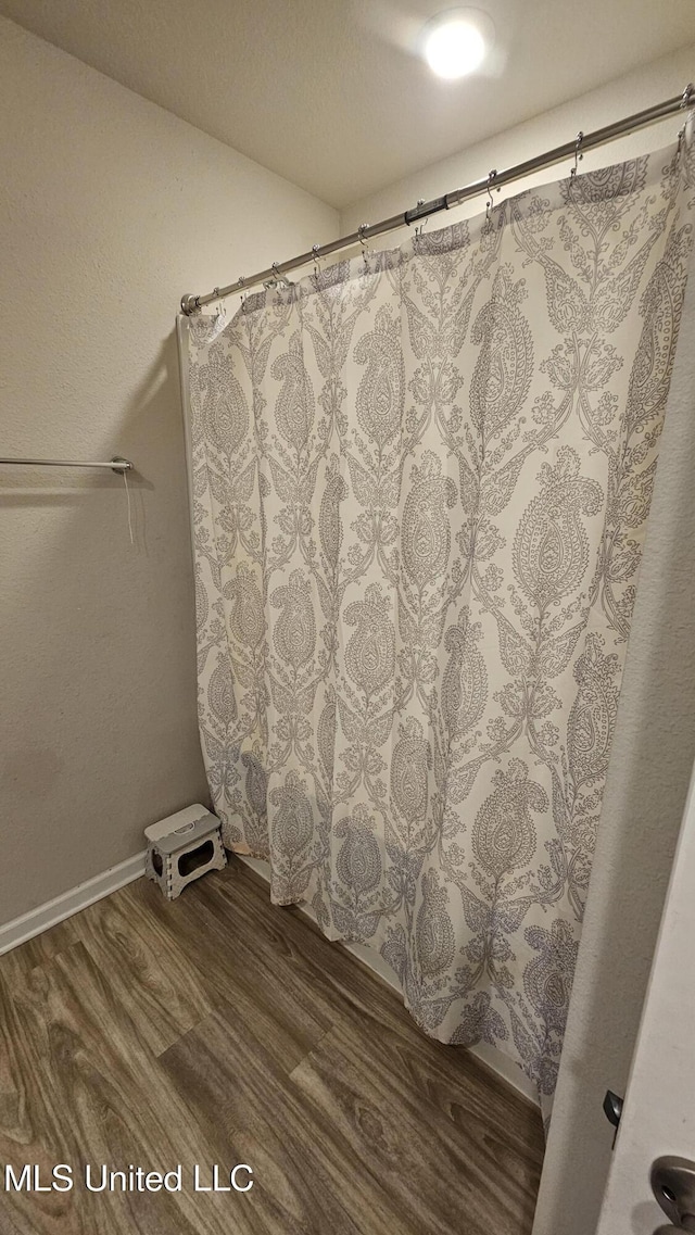 bathroom featuring baseboards, wood finished floors, and a shower with shower curtain