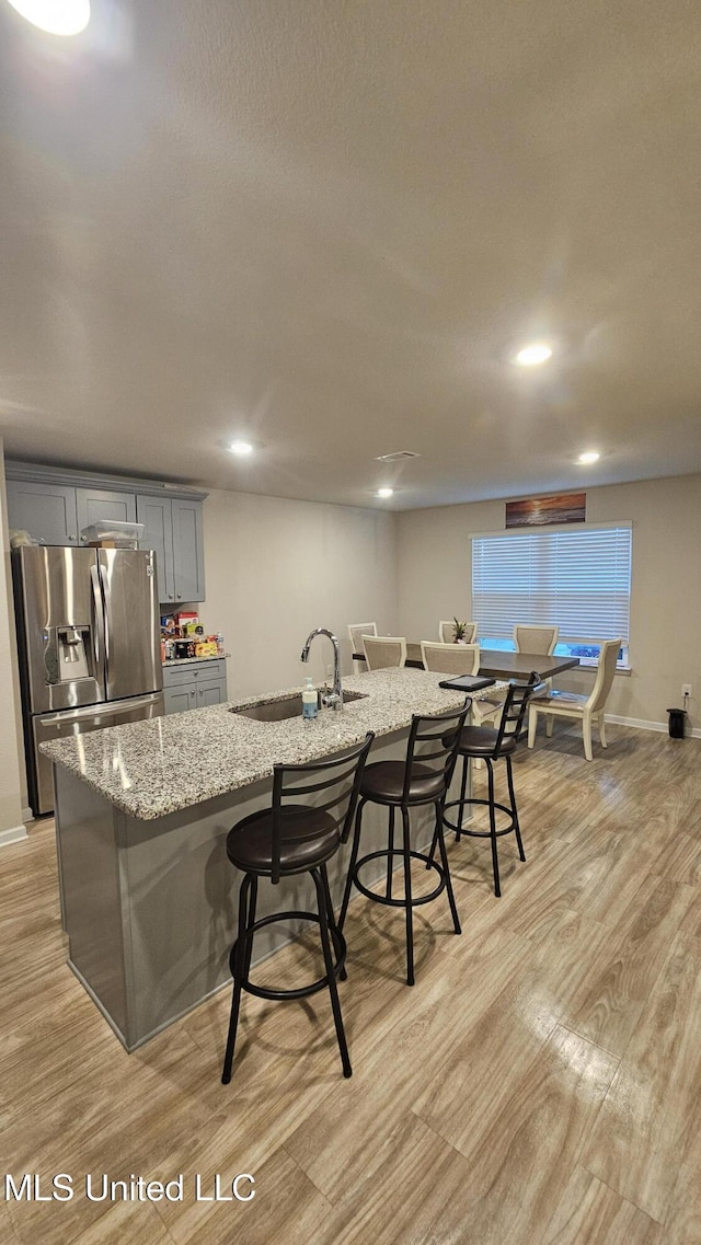 kitchen featuring a breakfast bar area, stainless steel fridge, light wood-style floors, a sink, and gray cabinetry