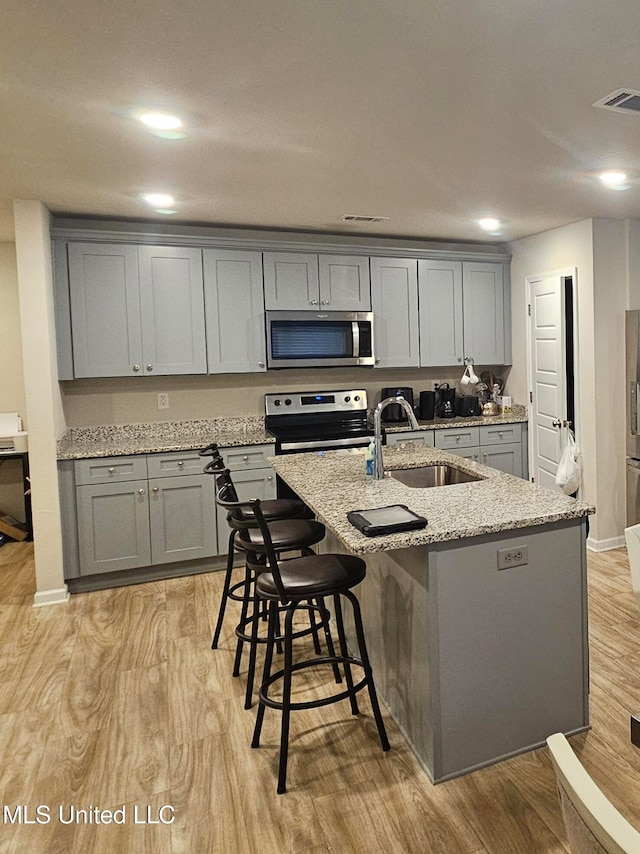 kitchen featuring appliances with stainless steel finishes, light hardwood / wood-style flooring, sink, and an island with sink