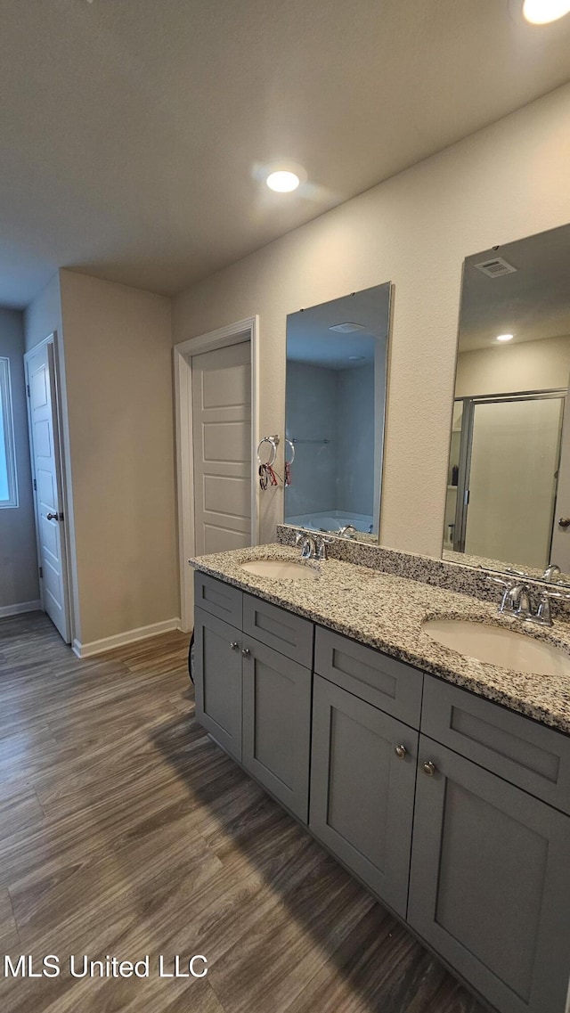 bathroom with double vanity, wood finished floors, a shower stall, and a sink